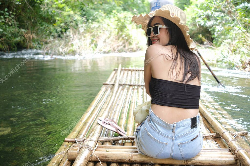 Beautiful young woman travel by bamboo raft along the stream on summer vacation and relaxation of leisure activity