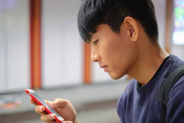 Young handsome asian man looking at cellphone checking social media, surfing internet, ordering food delivery, using mobile apps at weekend at subway