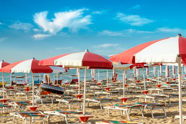 Red and white umbrellas and sunlongers on the sandy beach — Stock Photo, Image