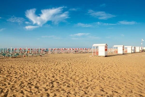 Parapluies rouges et blancs et parasols sur la plage de sable — Photo