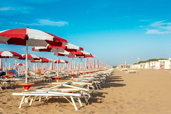 Red and white umbrellas and sunlongers on the sandy beach — Stock Photo, Image