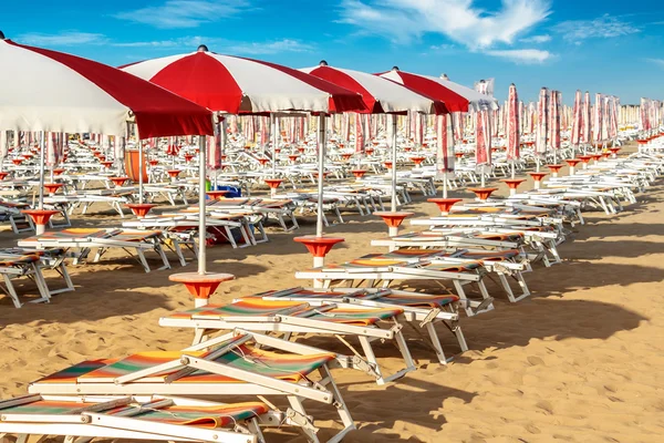 Red and white umbrellas and sunlongers on the sandy beach — Stock Photo, Image