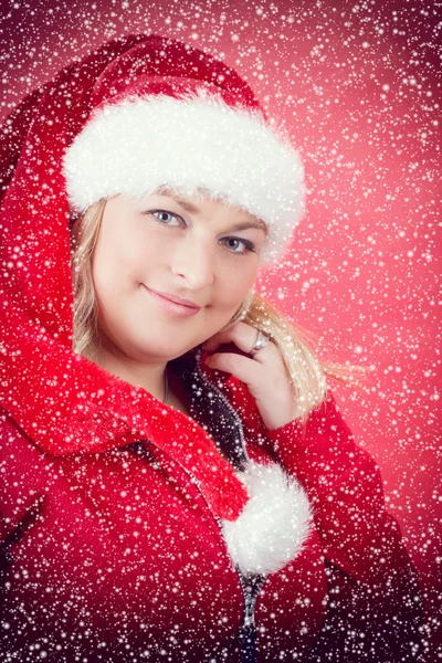 Joyful pretty woman in red santa claus hat smiling with snowflakes — Stock Photo, Image