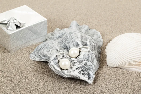 Two pearl earrings and shells on sand — Stock Photo, Image