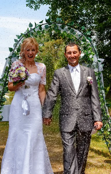 Happy just married couple under a rice rain — Stock Photo, Image