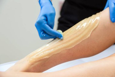 Profesyonel şekerci müşterinin bacağına balmumu sürüyor.