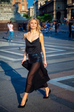 Çekici genç sarışın kız Milano 'da uzun siyah gece elbisesi içinde yürüyor ve poz veriyor.