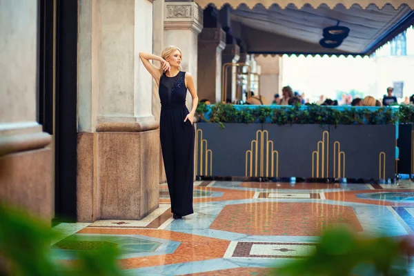 Çekici genç sarışın kız Milano 'da uzun siyah bir takım elbiseyle dolaşıyor ve poz veriyor.