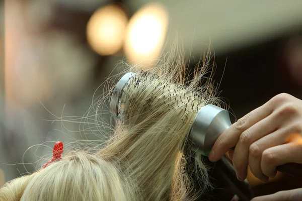Парикмахер расчесывает волосы расчёской и феном — стоковое фото
