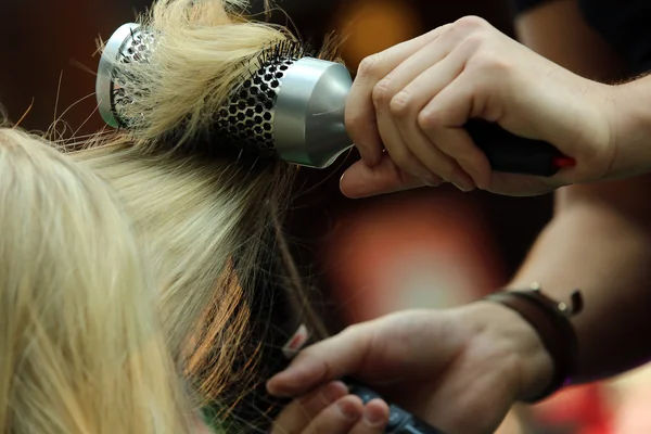 Парикмахер расчесывает волосы расчёской и феном — стоковое фото