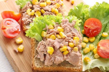 Sandwich with tuna and corn on wood background clipart