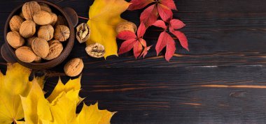 Ahşap zemin üzerinde ceviz ve akçaağaç yaprakları olan bir kase. Sonbahar konsepti.