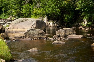Big Boulders in the Au Sable River on a sunny summer afternoon, surrounded by trees and moving water, Lake Placid New York.