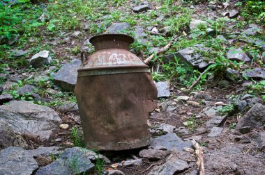 View of an abandoned old rusted metal milk can sitting out in the wilderness on rocks.