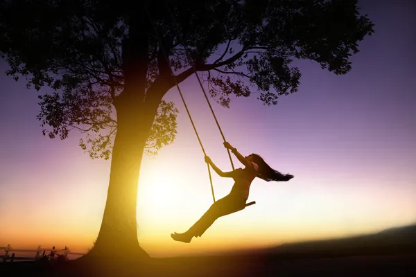 Silueta de la joven feliz en un columpio con fondo puesta de sol Imágenes De Stock Sin Royalties Gratis