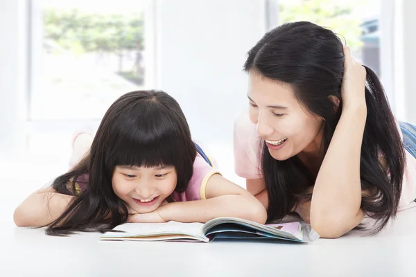 Junge Mutter und ihre Tochter liegen auf dem Boden und lesen ein Buch — Stockfoto