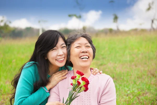 Senyum putri dan ibunya dengan bunga anyelir di gra — Stok Foto