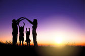 glückliche Familie macht Hausschild auf dem Hügel mit Sonnenaufgang Hintergrund