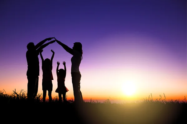 Glückliche Familie macht Hausschild auf dem Hügel mit Sonnenaufgang Hintergrund — Stockfoto