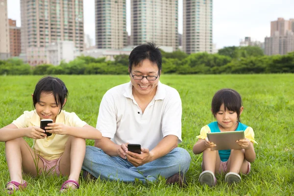 Familia feliz usando el teléfono inteligente y la tableta PC al aire libre — Foto de Stock