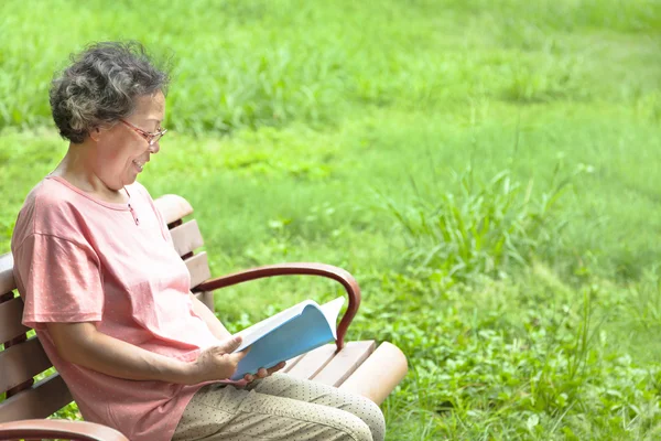 Felice donna anziana seduta sulla panchina e leggere un libro — Foto Stock