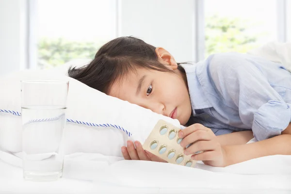 Niña enferma sosteniendo la medicina en la cama — Foto de Stock