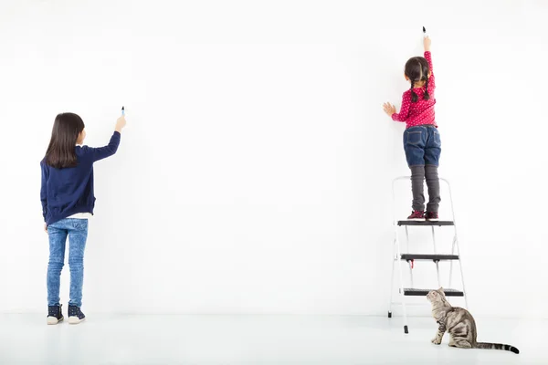 Two kids drawing on the blank white wall — Stock Photo, Image