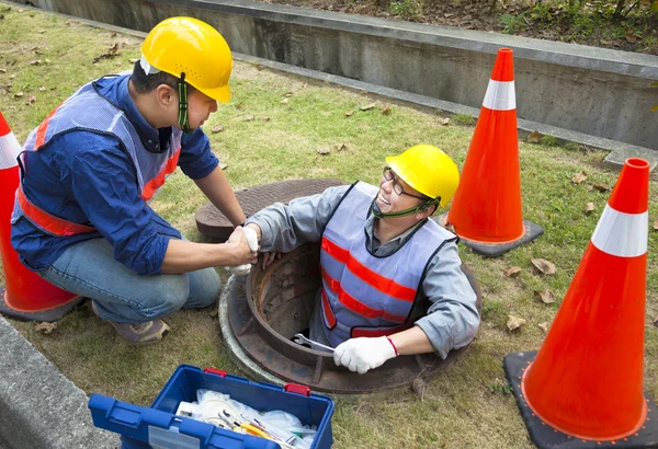 Dos trabajadores de alcantarillado en la boca de inspección —  Fotos de Stock