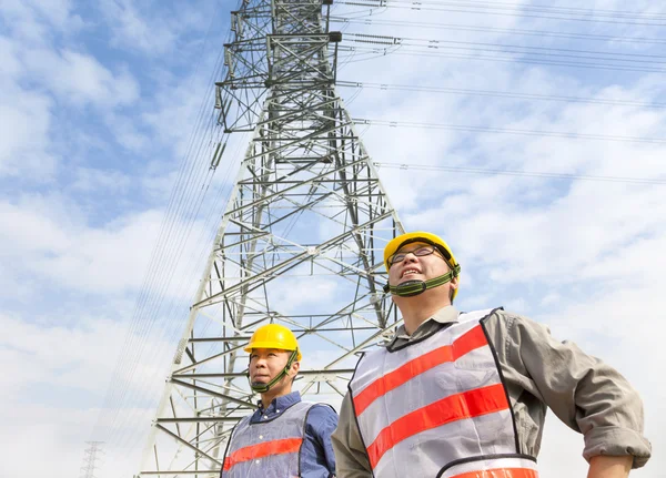 Dois trabalhadores em pé diante da torre de energia elétrica — Fotografia de Stock