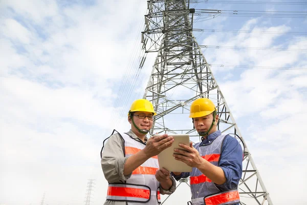 Dos trabajadores de pie ante la torre de energía eléctrica —  Fotos de Stock