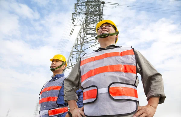 Два работника, стоящие перед электрической башней — стоковое фото