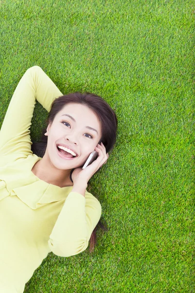 Mujer joven sonriente acostada con teléfono celular en el prado verde —  Fotos de Stock