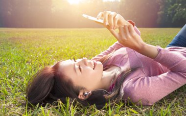 smiling young woman touching cell phone and lying on meadow clipart