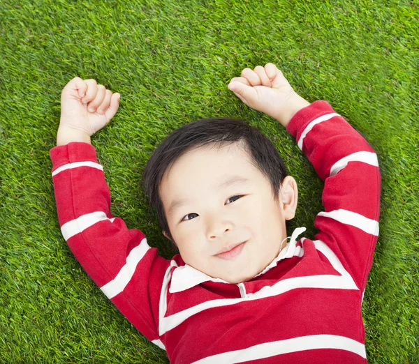 Petit garçon souriant se reposant et la main dans la prairie — Photo