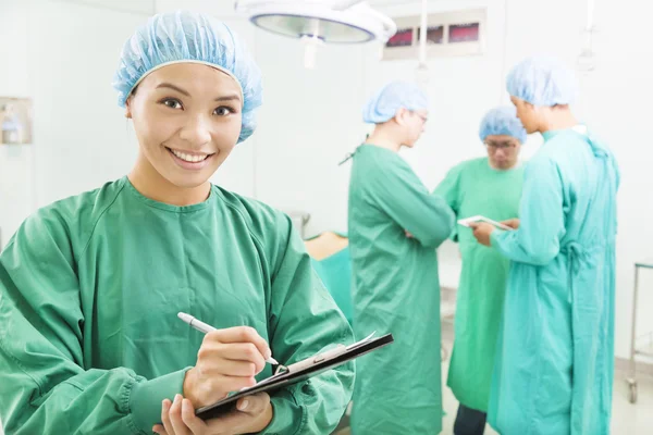 Gülümseyen kadın cerrahlar hasta ameliyat kayıtlarını yazma — Stok fotoğraf