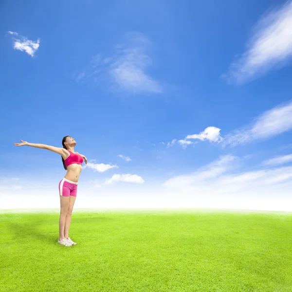 Расслабляющая молодая женщина стоит на лугу с голубым небом — стоковое фото