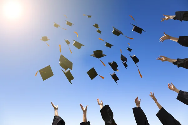 Felices jóvenes graduados lanzando sombreros — Foto de Stock