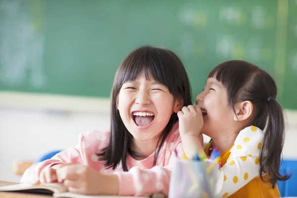 Смеющиеся маленькие девочки делятся секретами в классе — стоковое фото