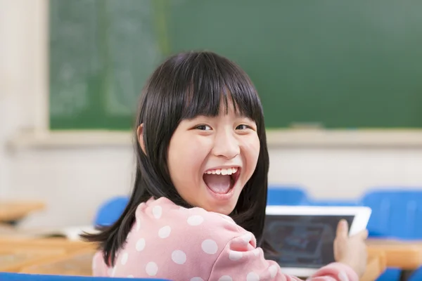 Pequena colegial feliz segurando tablet digital na mesa — Fotografia de Stock