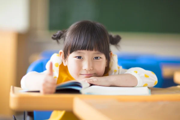 Lächelndes Kind liegt geneigt auf einem Schreibtisch und Daumen hoch — Stockfoto