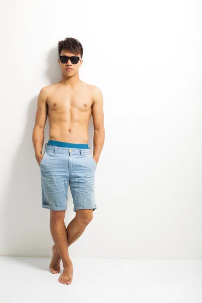 Ung man bär en solglasögon och står nära väggen — Stockfoto