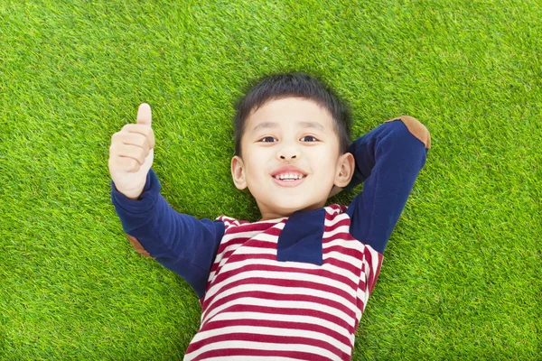 Glückliches Kind liegt und hebt den Daumen auf einer Wiese — Stockfoto