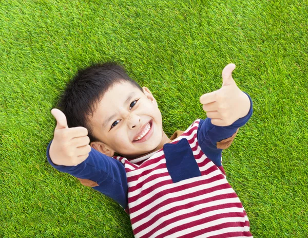 Lächelndes Kind liegend und Daumen hoch auf einer Wiese — Stockfoto