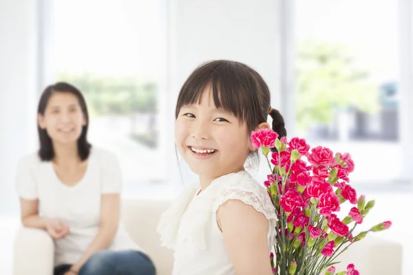 Little girl looking back and hiding a bouquet of carnations — Stock Photo, Image