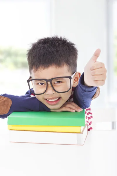 Kleiner Junge liegt auf Büchern und Daumen hoch — Stockfoto