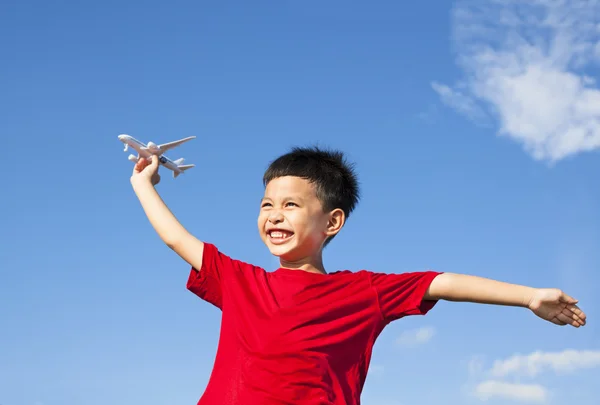 Niño feliz sosteniendo un juguete de avión con fondo de cielo azul — Foto de Stock