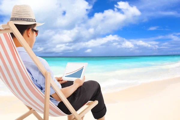 Geschäftsmann sitzt auf Strandstühlen und schaut auf die Börse — Stockfoto