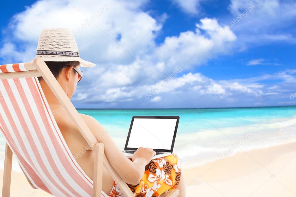 relaxed man sitting on beach chairs and using a laptop.
