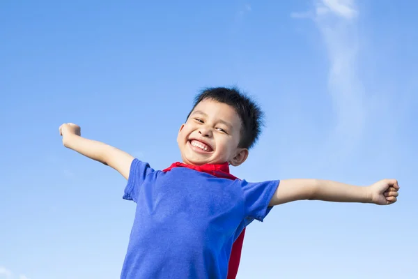 Glücklicher kleiner Junge imitiert Superhelden und Arme mit blauem Himmel — Stockfoto