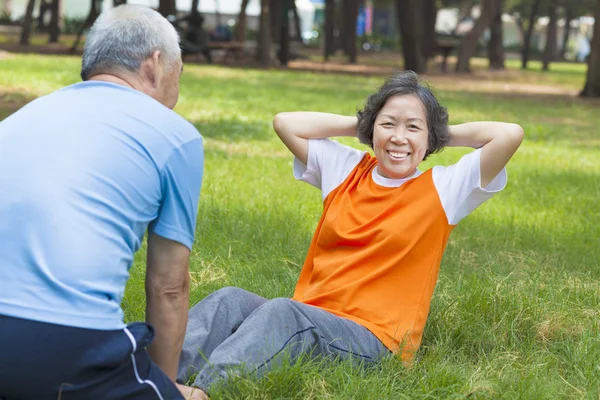Smiling senior grandmother doing sit-ups in the park — Stock Photo, Image